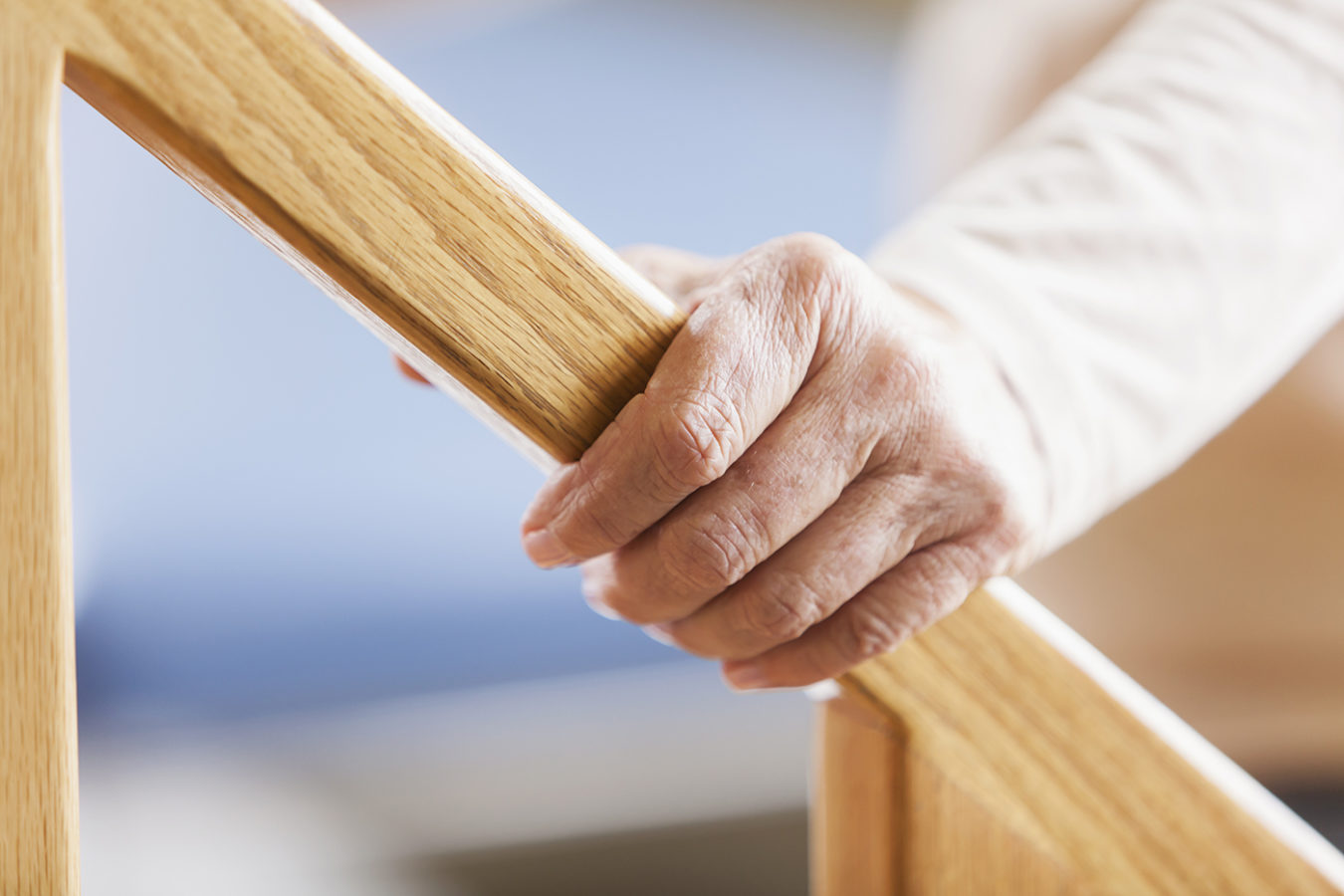 A senior woman's hand placed on an oak stair rail.
